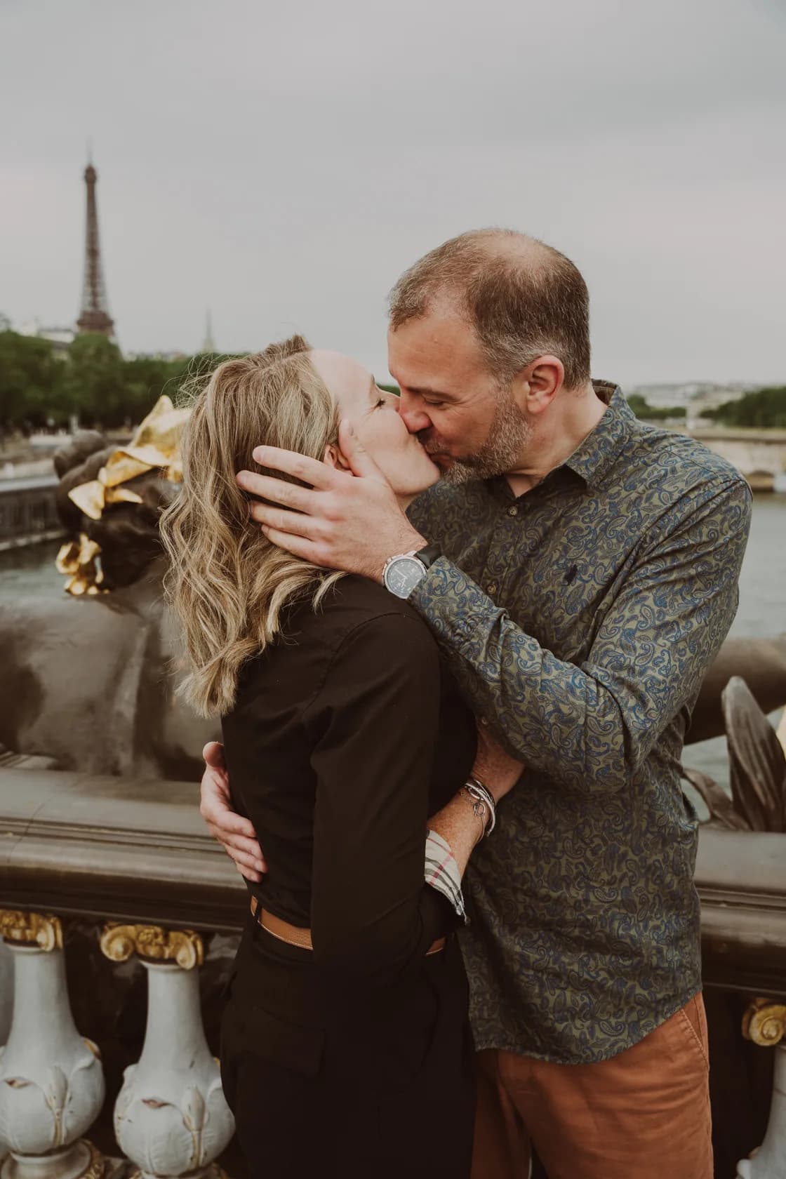 A couple kisses on the Alexandre III bridge, with the Eiffel Tower in the background.
