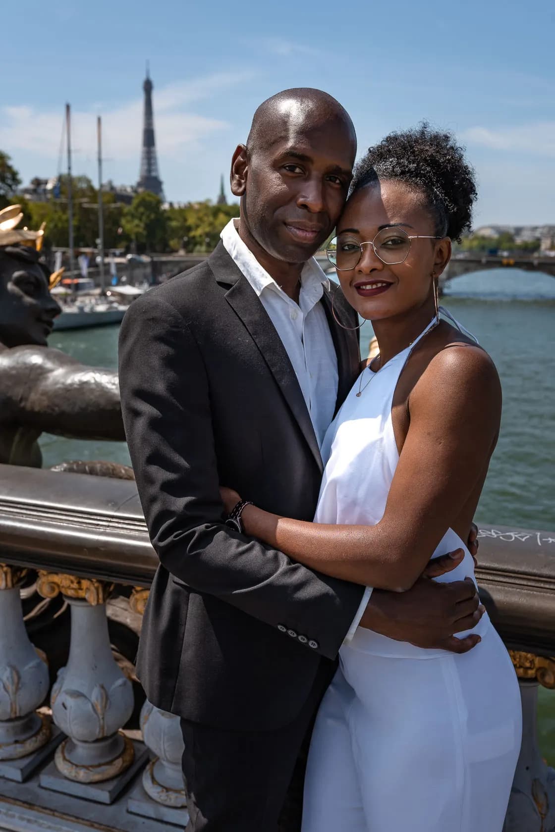 A couple embracing on the Alexandre III bridge, with the Eiffel Tower and the sunny Seine in the background.