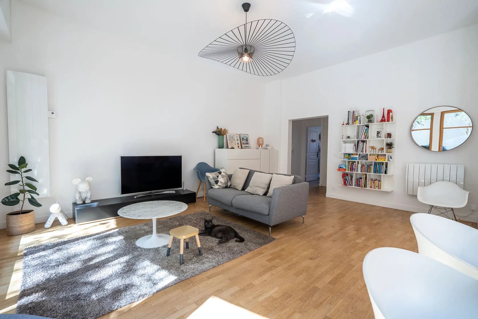 Vaste séjour lumineux, canapé gris, parquet chêne, chat noir lové sur le tapis