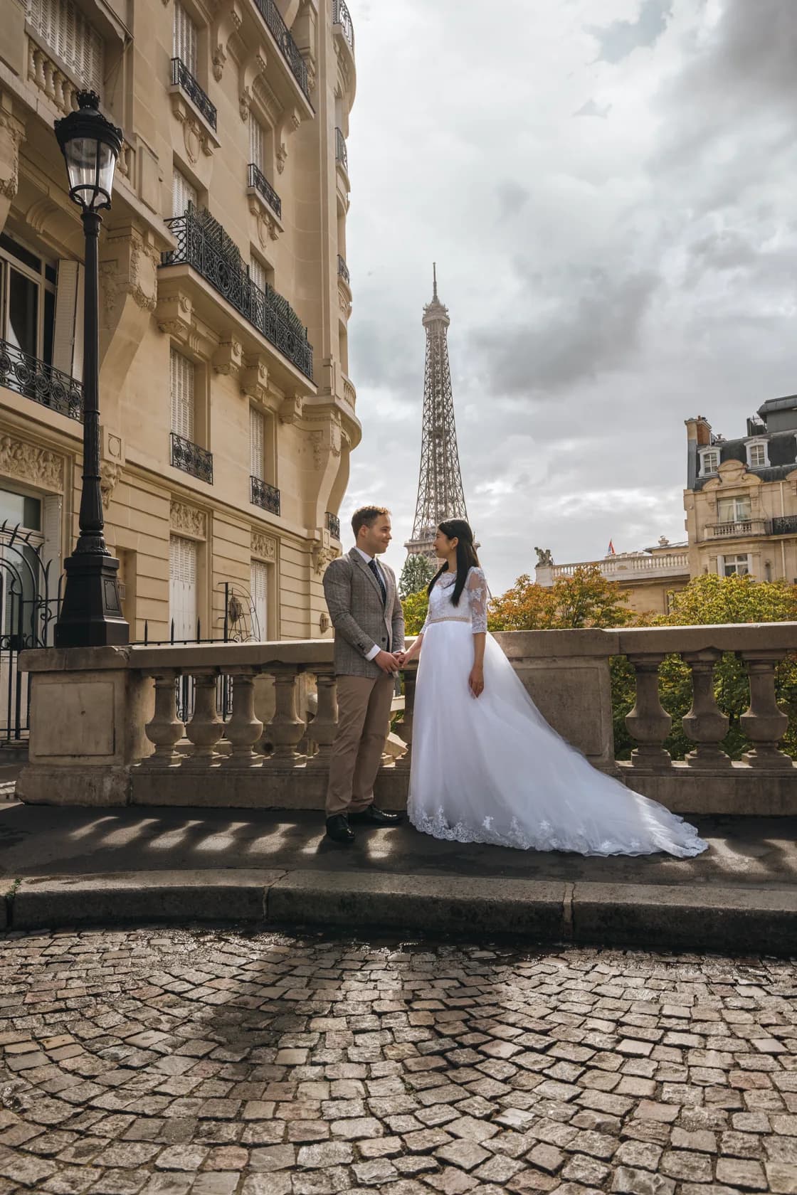 Les mariés de profil sur l'avenue de Camoëns, vue complète sur la Tour Eiffel entre les façades parisiennes