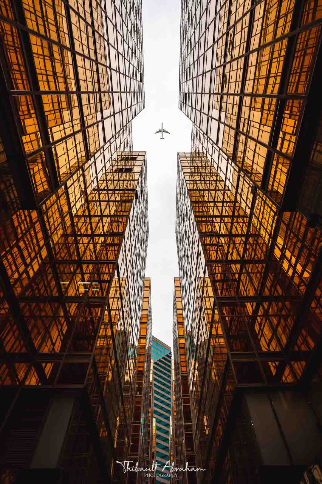Un avion survolant des buildings symétriques en verre orangé à Hong Kong