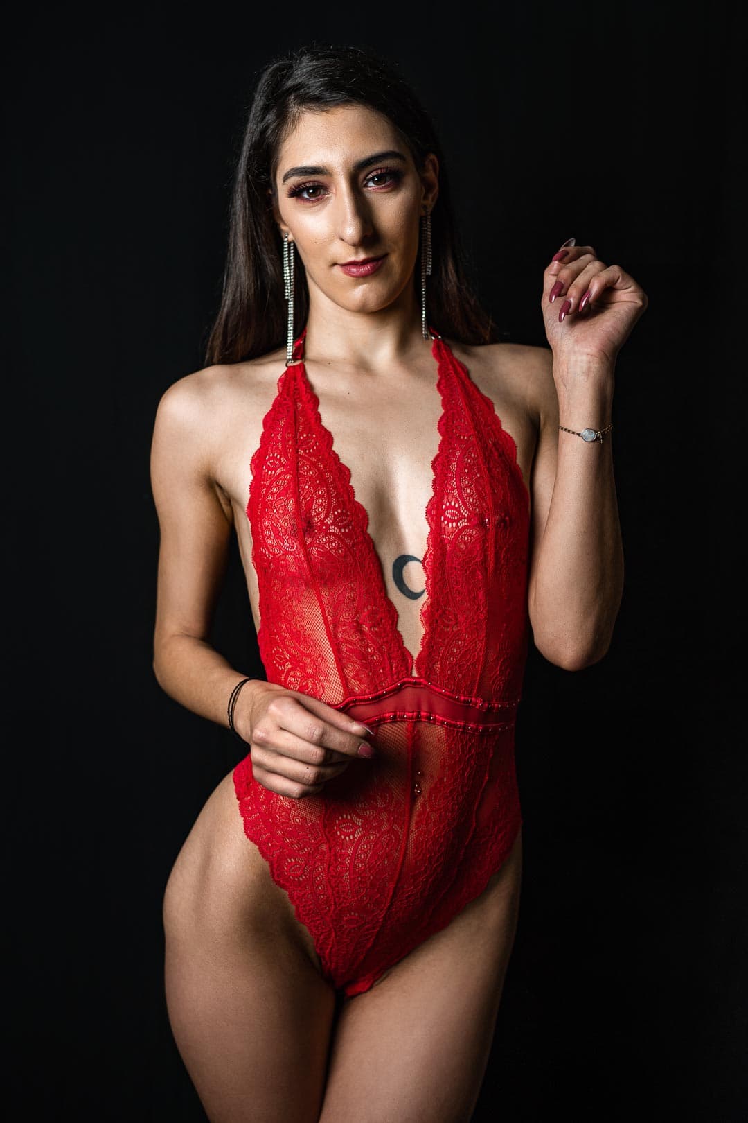 Femme en body rouge en dentelle posant sur fond noir
