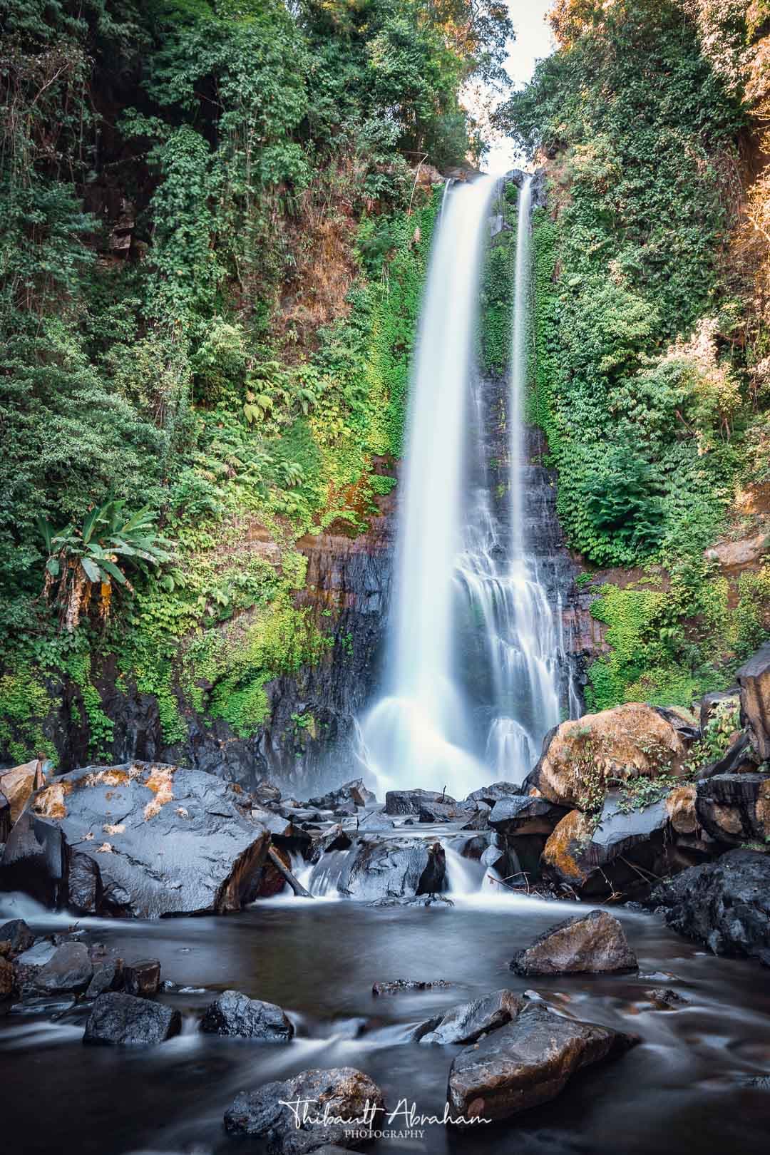 Plan large et effet de fluidité de la cascade Gitgit qui s'écrase sur les rochers, dans un environnement luxuriant à Bali