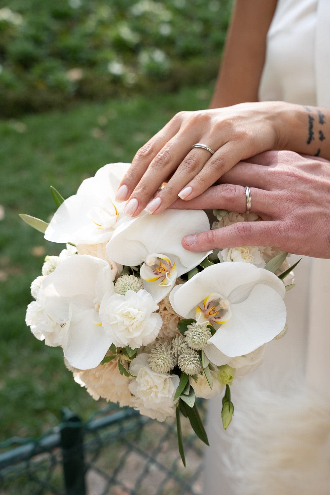 Détail d'un bouquet d'orchidées blanches, les mains des mariés posées dessus