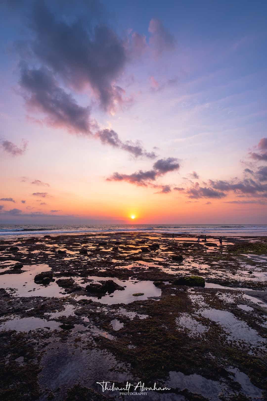 Coucher de soleil aux teintes violettes sur une plage de rochers à Bali