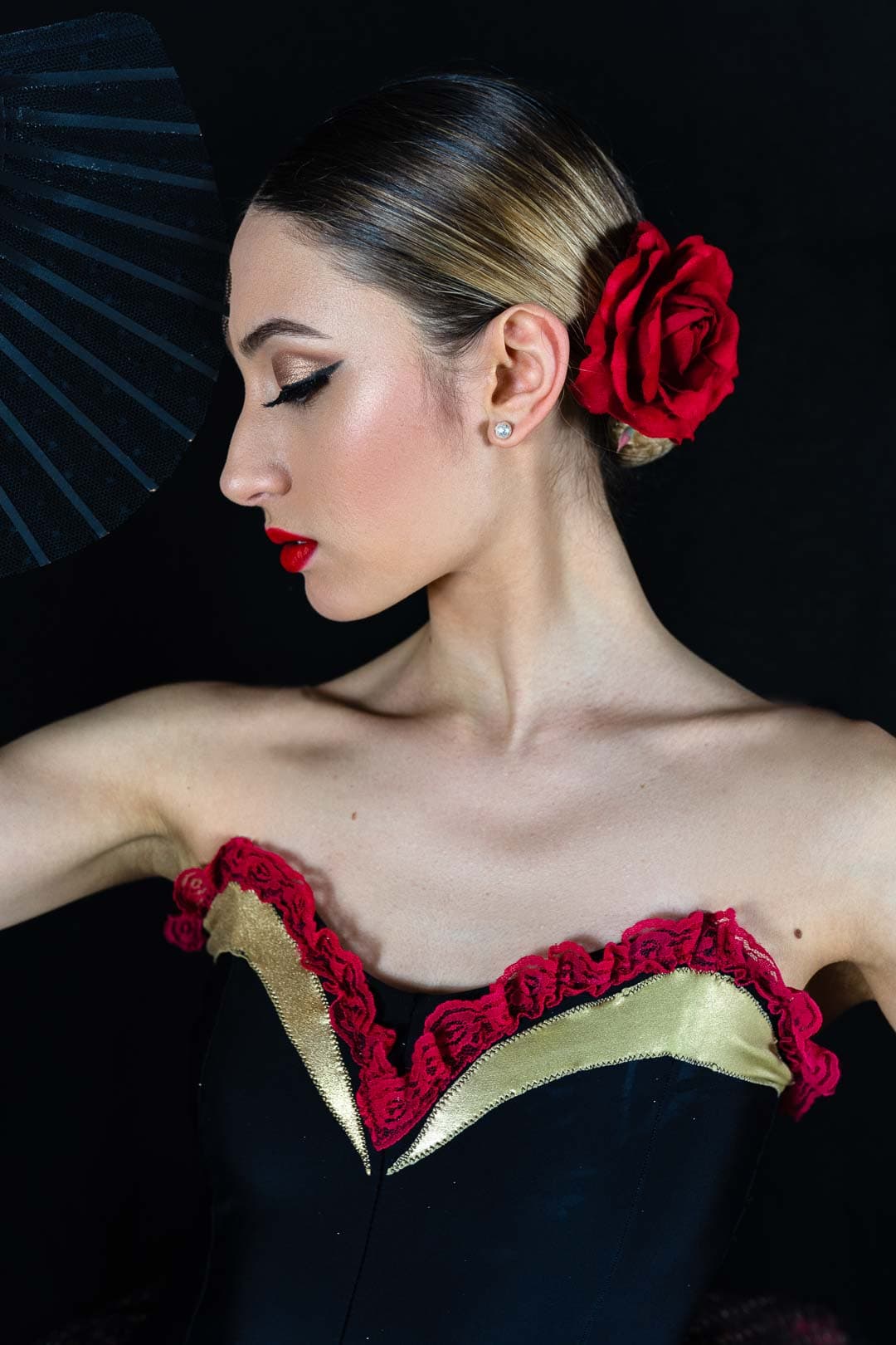 Portrait d'une danseuse de flamenco avec une rose rouge dans les cheveux, un maquillage sophistiqué et un éventail noir en arrière-plan
