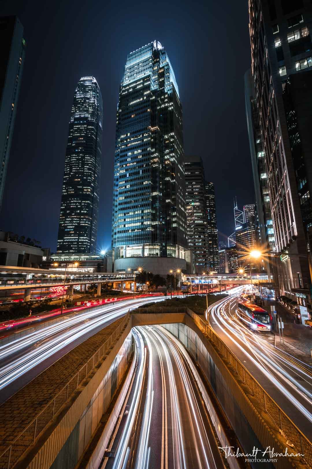 Skyline du quartier financier de Hong Kong la nuit, traînées lumineuses des voitures en premier plan
