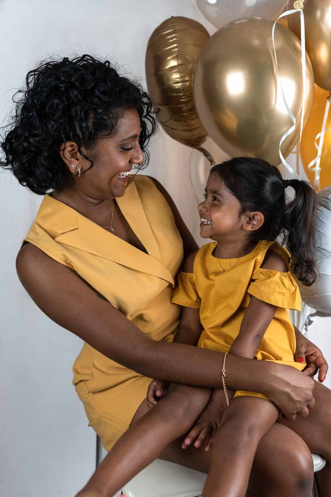 Mère et fille souriantes en tenues jaunes, entourées de ballons dorés et argentés