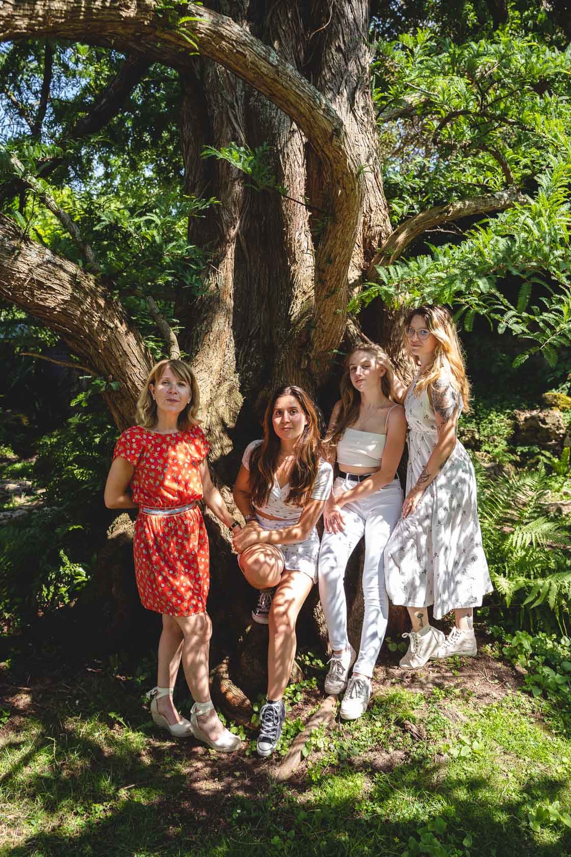 Trois sœurs et leur mère posant ensemble au pied d'un grand arbre dans un parc verdoyant, un cadeau pour la fête des mères