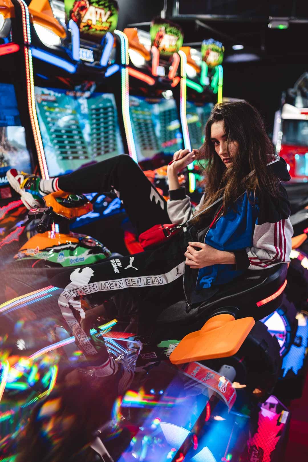 Jeune femme en jogging assise sur une machine retro gaming dans une salle d'arcade