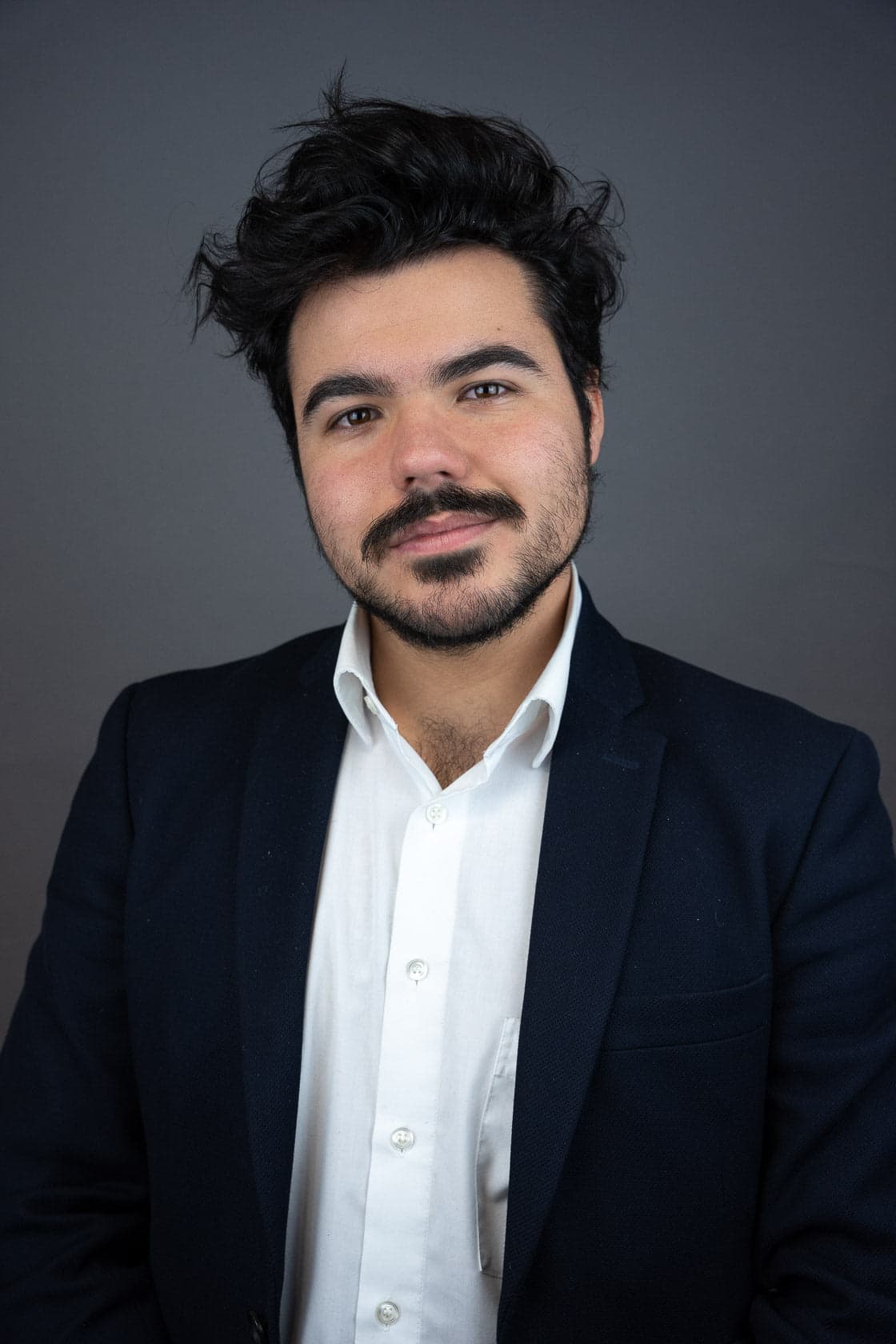 Portrait d'un jeune homme souriant, portant un blazer bleu marine sur une chemise blanche
