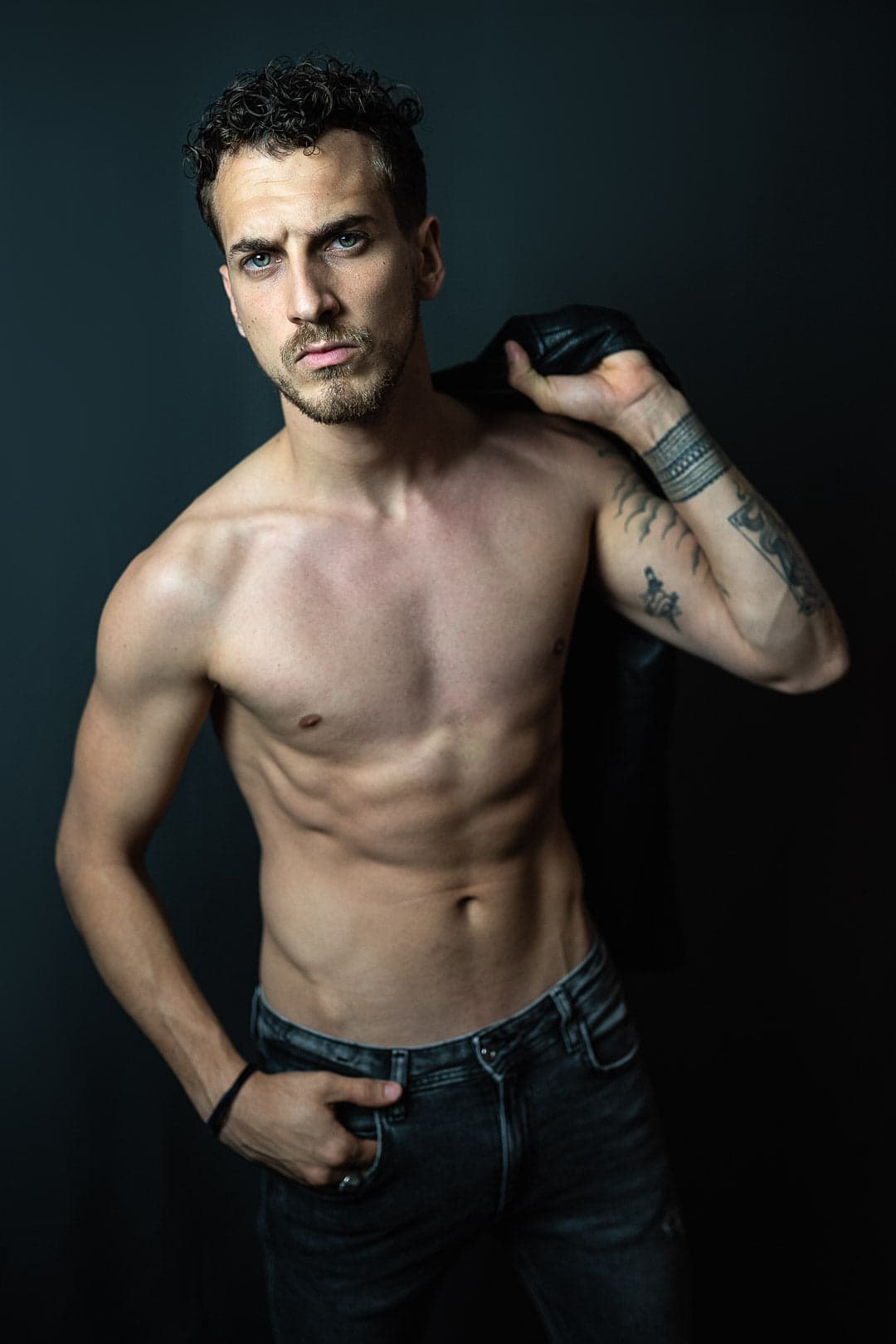 Modèle masculin torse nu avec une veste en cuir sur l'épaule, en studio sur fond gris