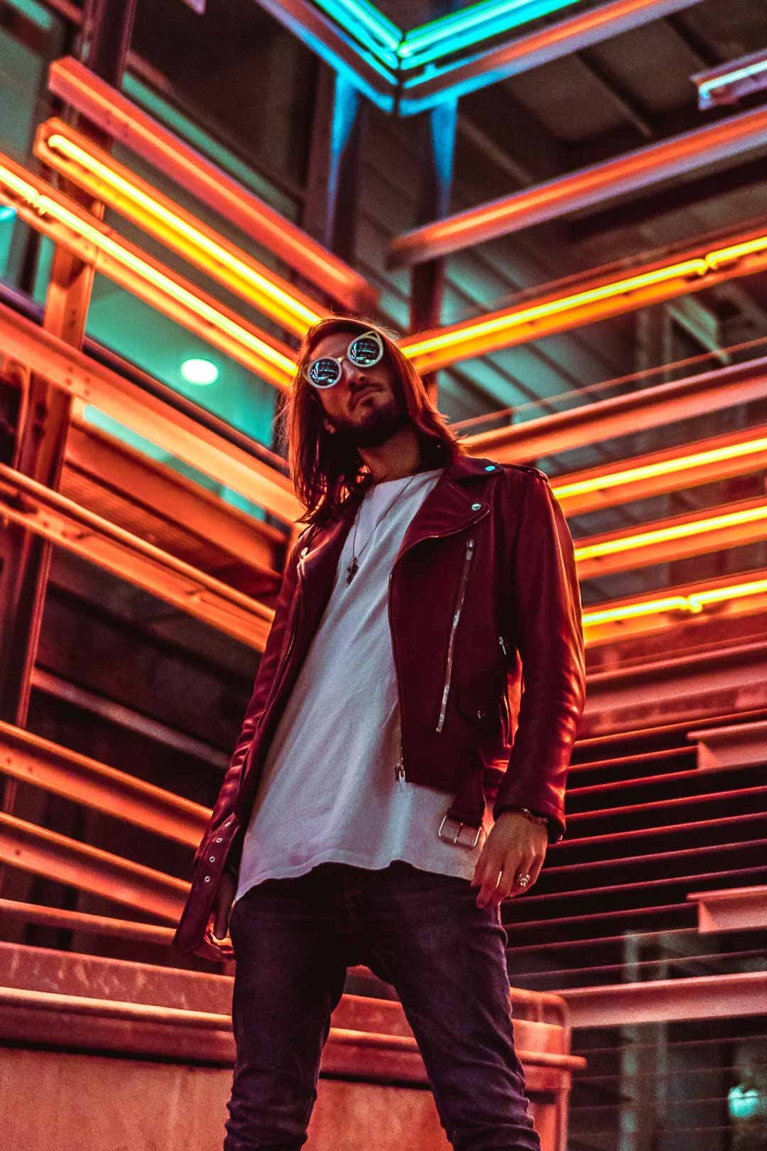 Homme portant une veste en cuir rouge, debout sous des lumières néon colorées dans un environnement urbain à Los Angeles