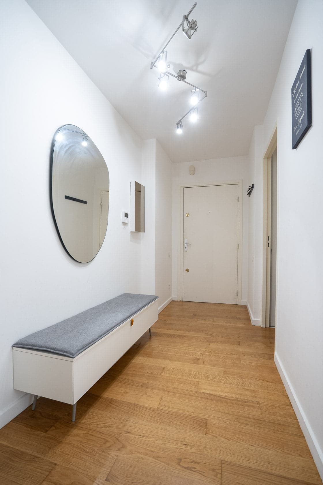 Entrée avec miroir rond, banquette grise et couloir parquet bois