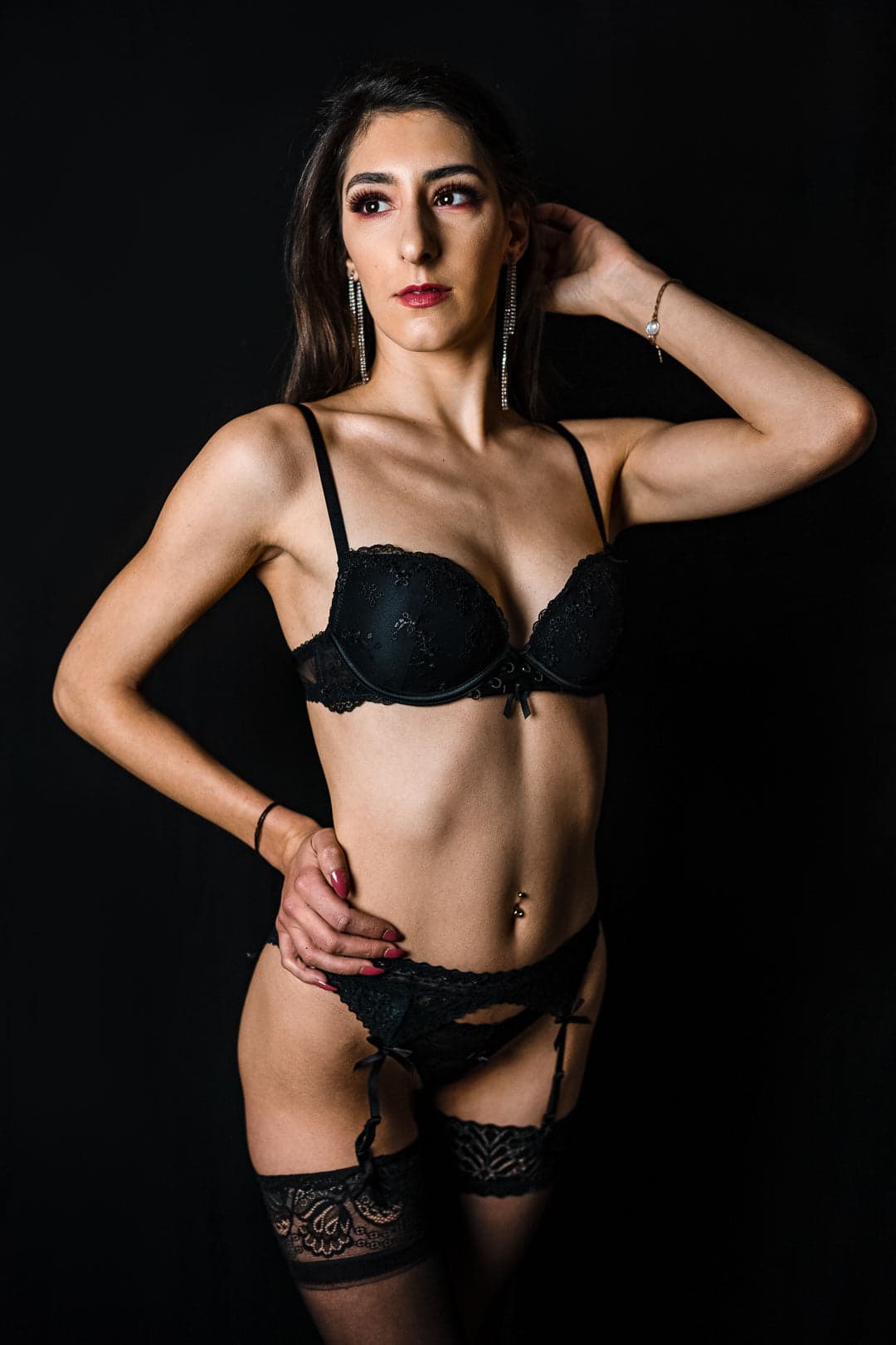 Femme en soutien-gorge et culotte noirs avec des bas jarretières, posant sur fond noir