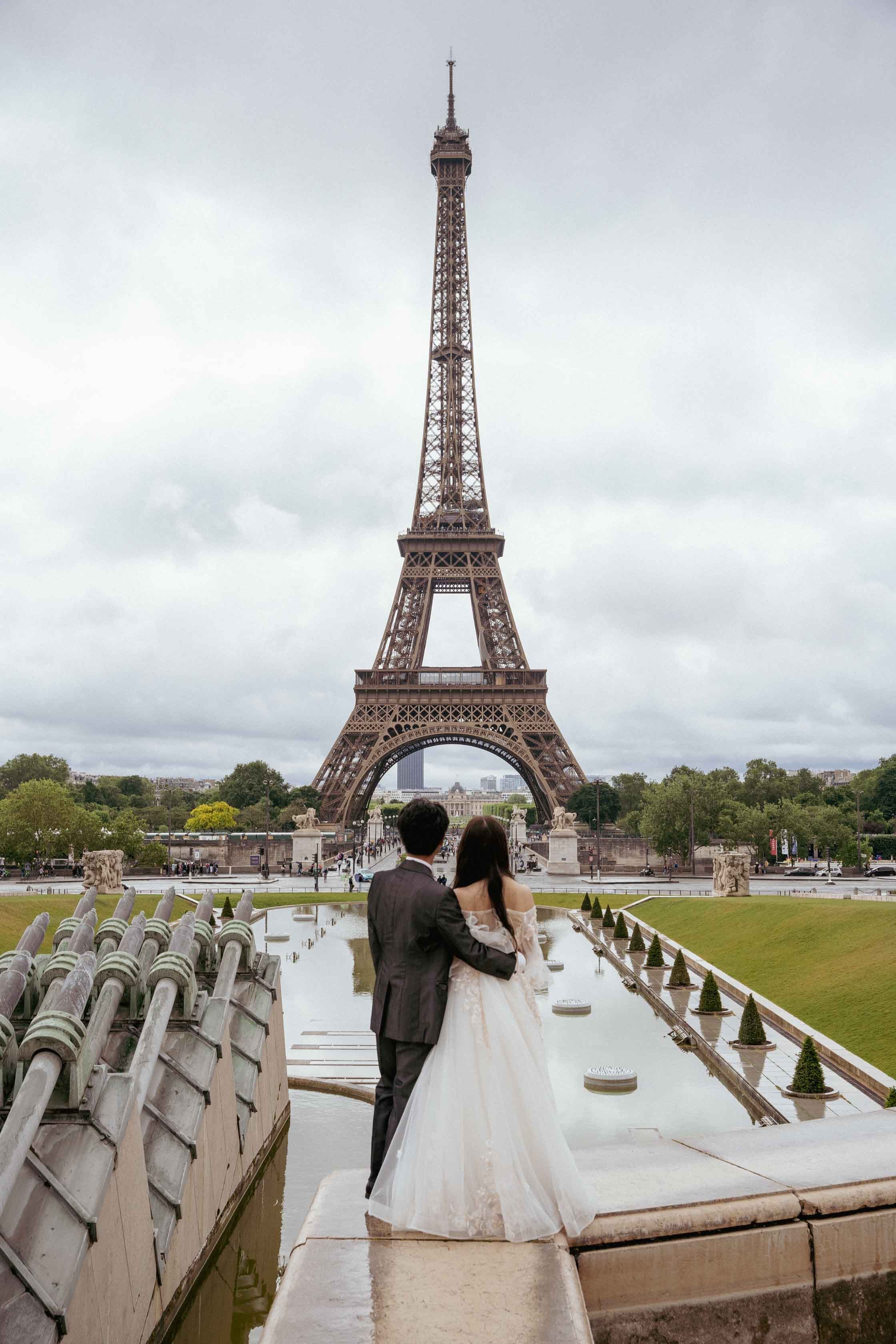 Les mariés vus de dos, enlacés face à la tour Eiffel, depuis les bassins du Trocadéro à Paris