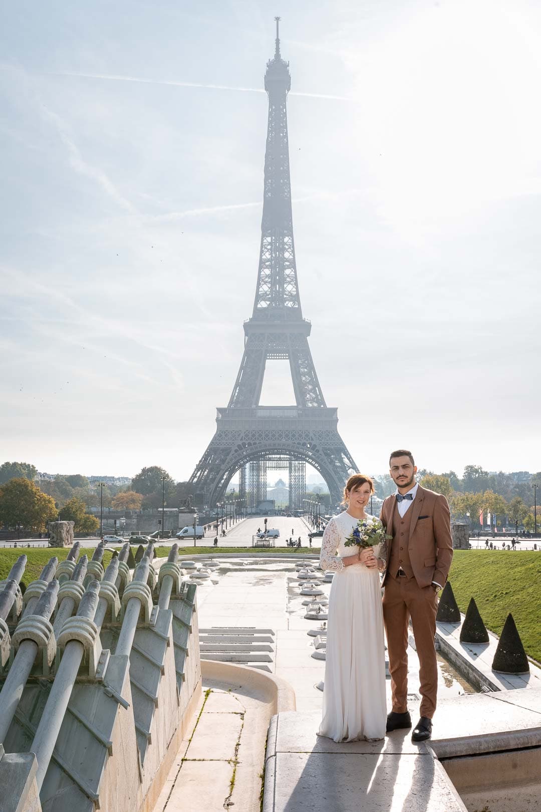 Les mariés se tenant la main devant la majestueuse Tour Eiffel, symbolisant l'amour dans un cadre iconique.