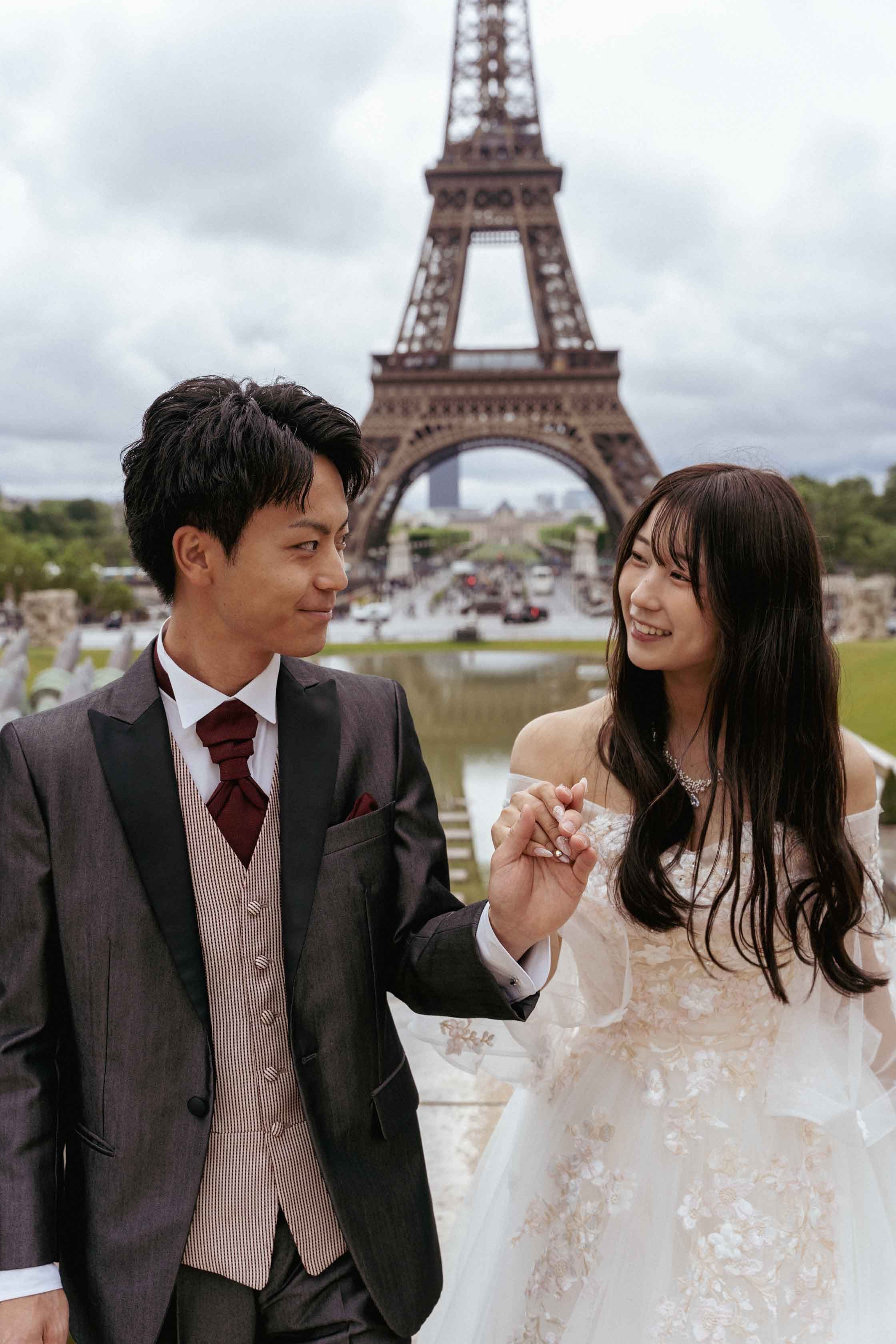 Les mariés se tenant la main, regards complices, Tour Eiffel en arrière-plan
