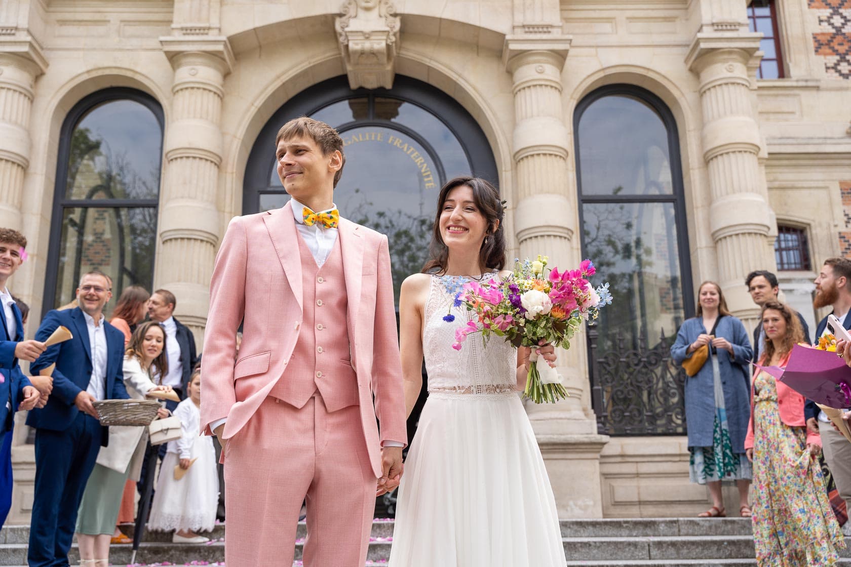 Les mariés, main dans la main, sortent de la mairie, entourés de leurs invités et rayonnants de bonheur.