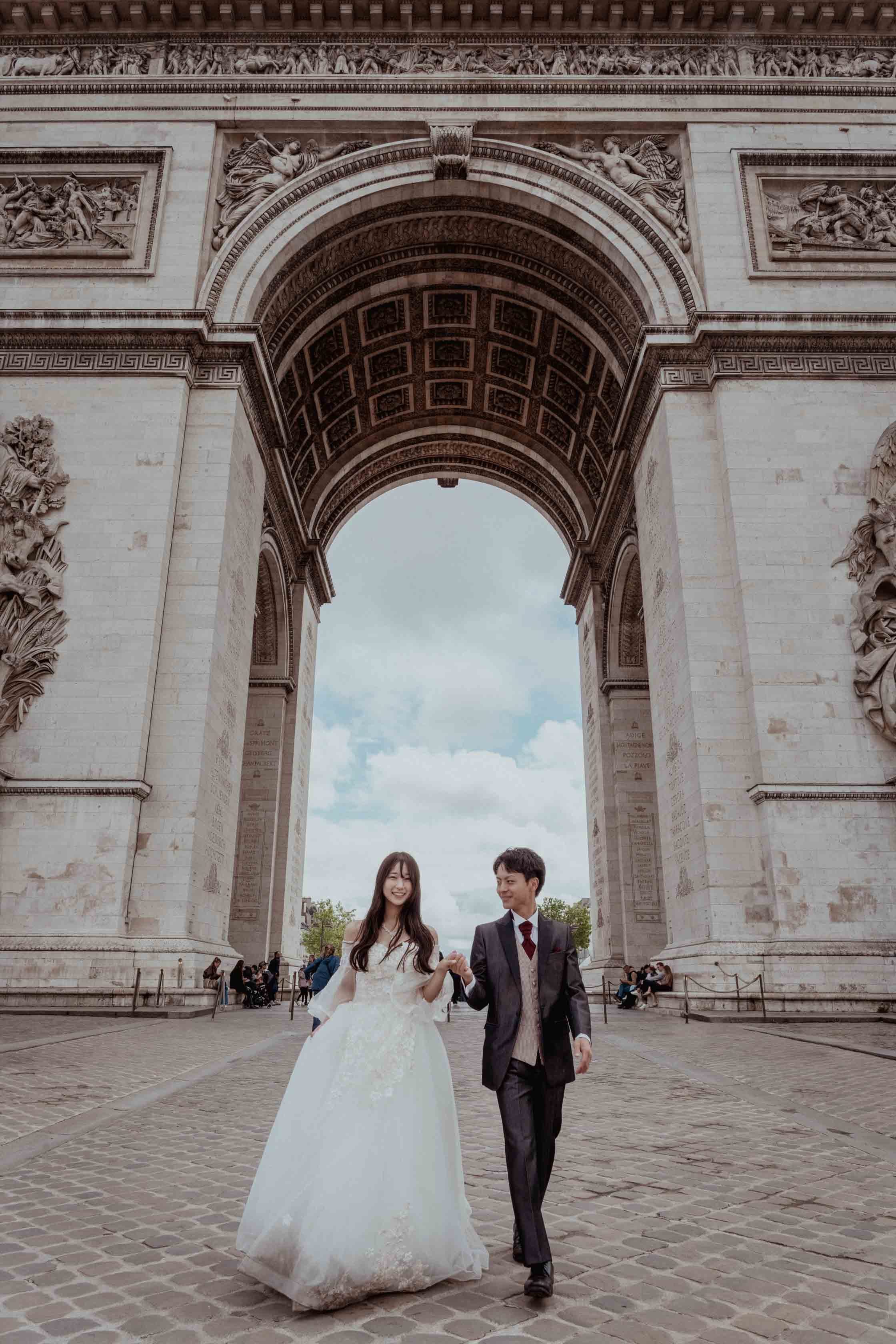 Les mariés marchent main dans la main sous la voûte de l'Arc de Triomphe, à Paris