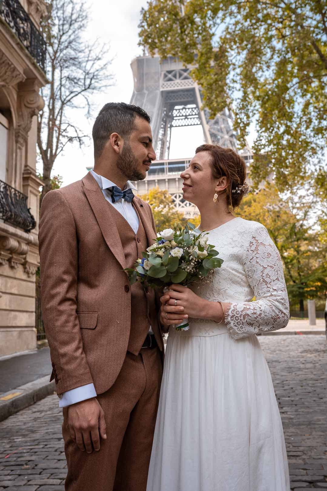 Mariés se regardant tendrement, la Tour Eiffel en arrière-plan, capturant un moment romantique.