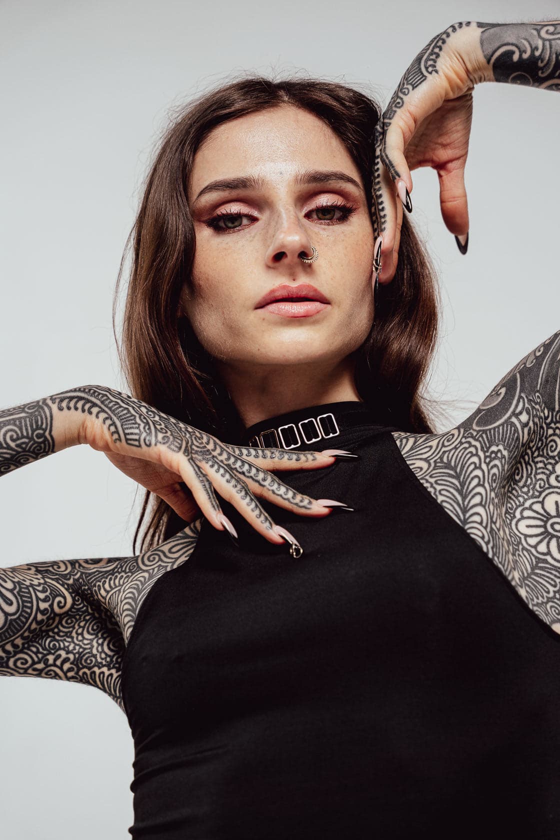 Portrait en studio de Noémie Doragon, haut noir à col montant, les mains levées au-dessus de la tête