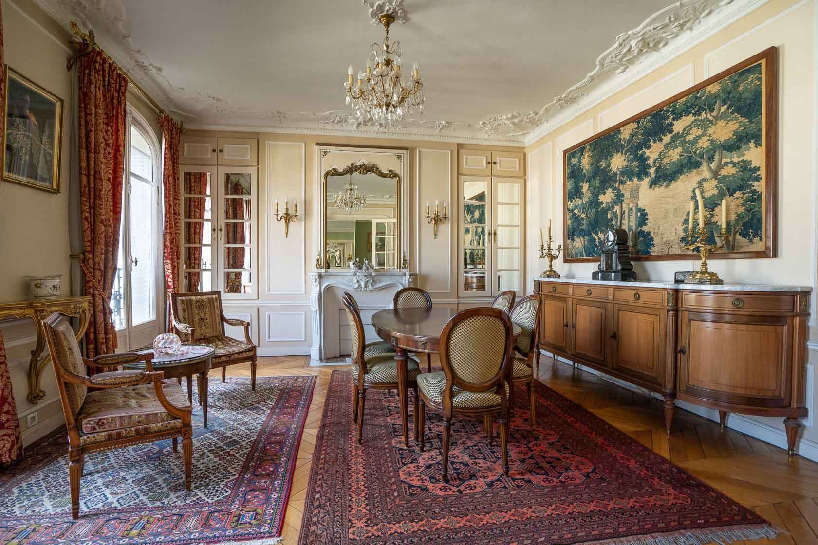 Pièce de réception élégante avec un long tapis rouge, une table à manger ovale et des chaises, donnant sur un balcon avec vue sur les toits de Paris