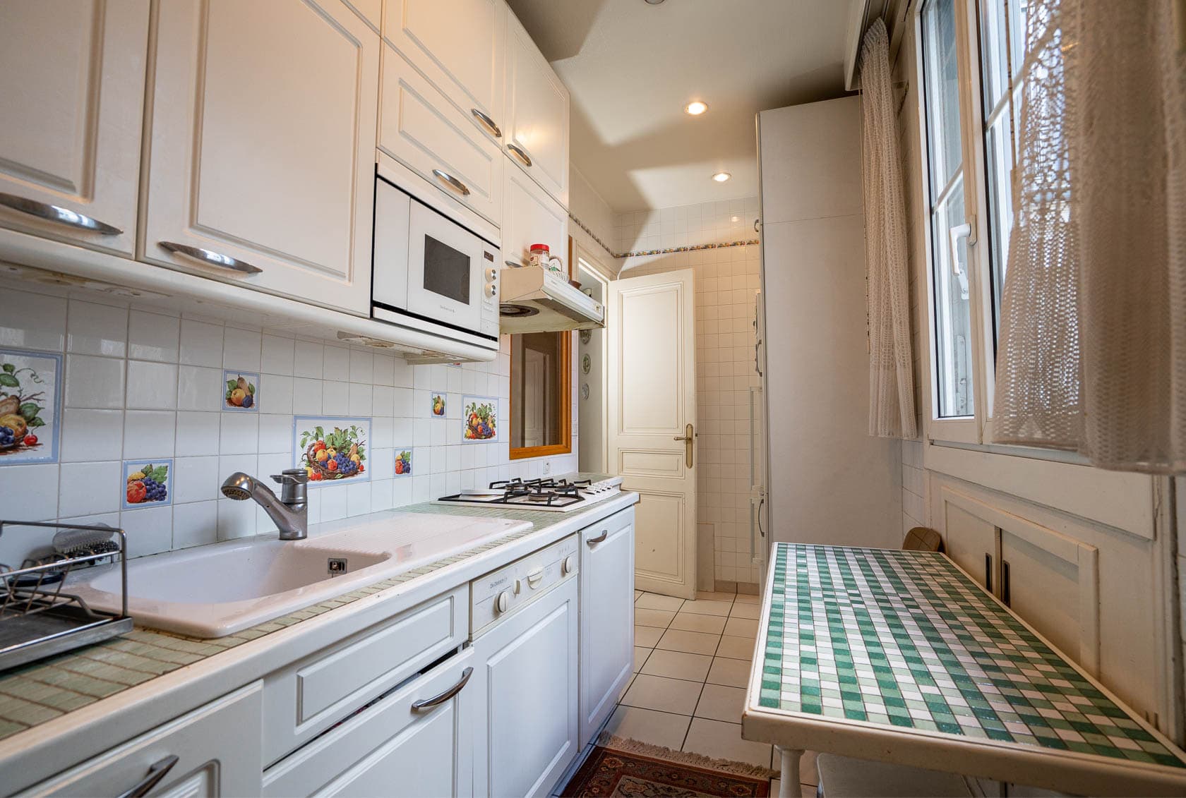 Cuisine blanche fonctionnelle avec un plan de travail en carrelage, un évier, une plaque de cuisson et un petit coin repas