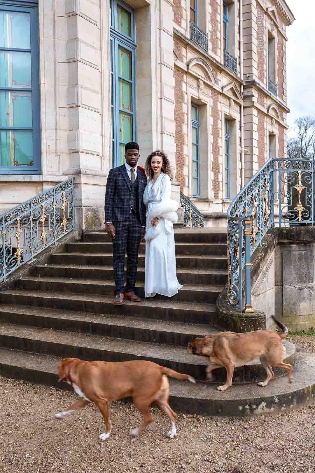 Les mariés accompagnés de leurs deux chiens sur les marches du château de Sceau, illustrant un moment familial et complice.