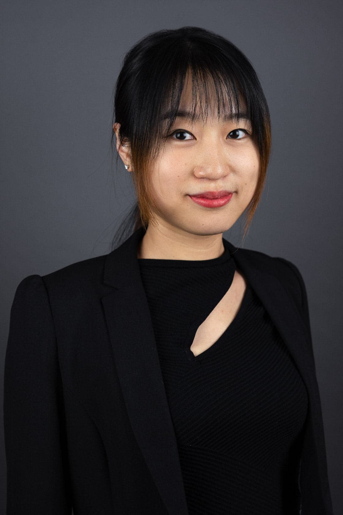 Portrait d'une jeune femme asiatique aux cheveux noirs avec frange, portant un blazer noir sur un haut noir à découpe
