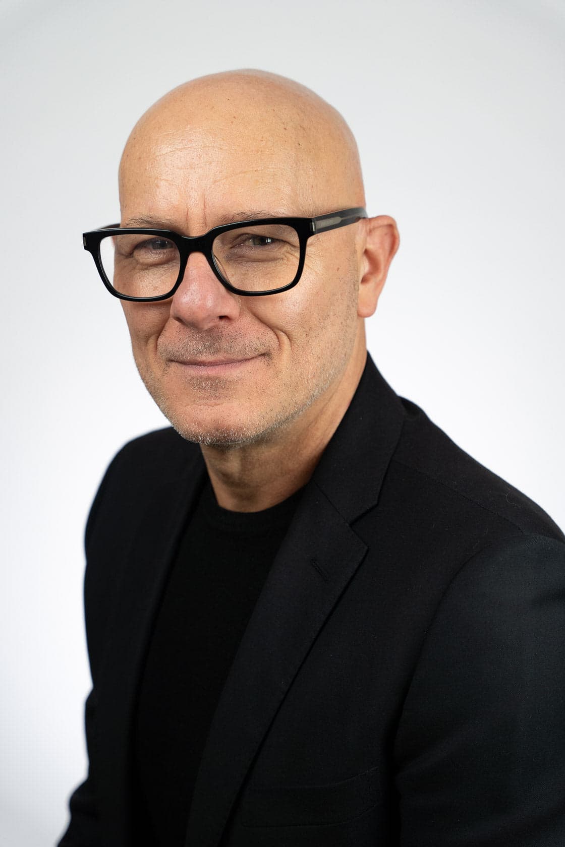 Portrait d'un homme chauve souriant portant des lunettes noires et un blazer noir sur un t-shirt noir