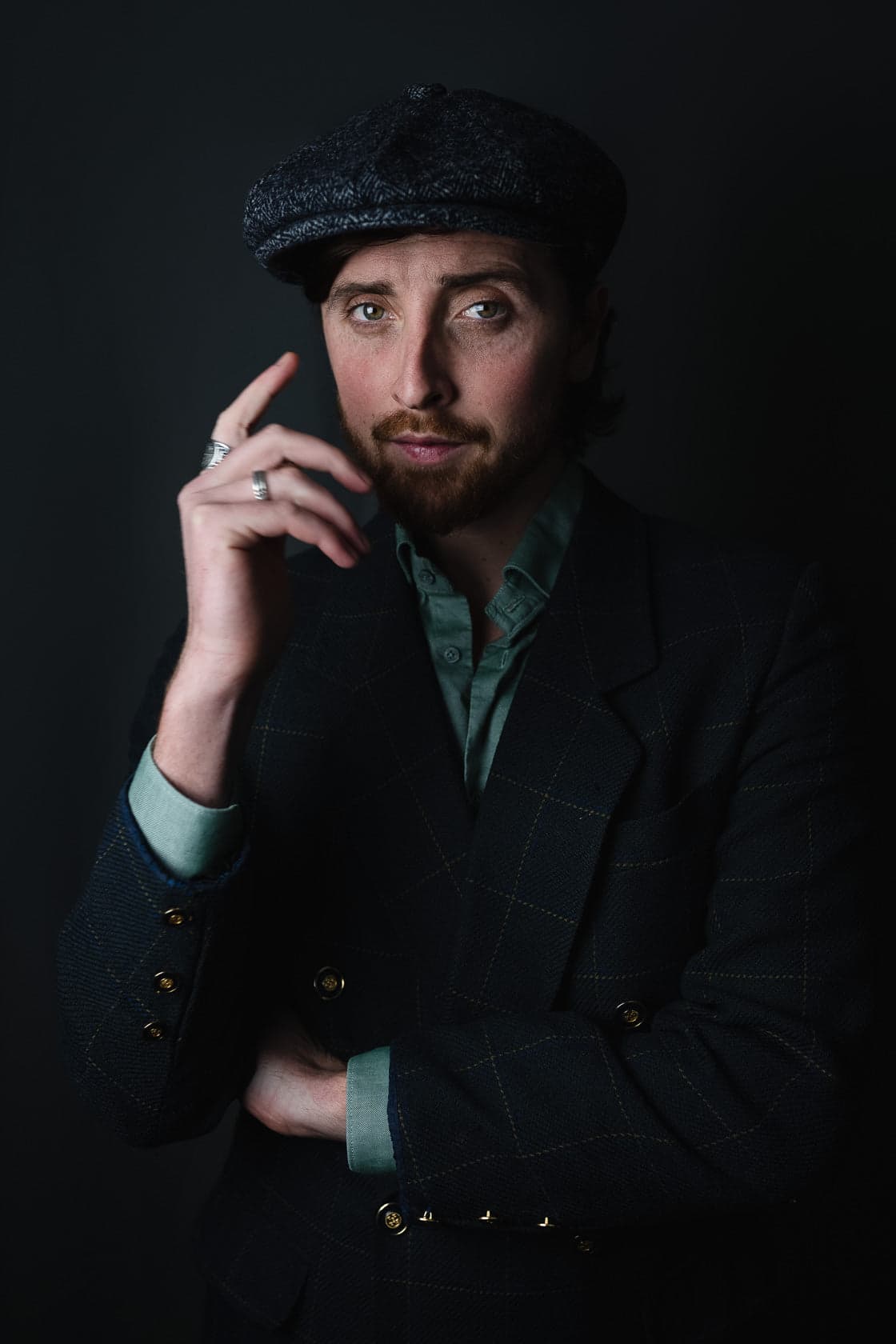 Portrait studio d'un homme en costume à carreaux adoptant une attitude détendue confiante, il porte une casquette à carreaux gris, une chemise vert clair et un blazer à carreaux sombres