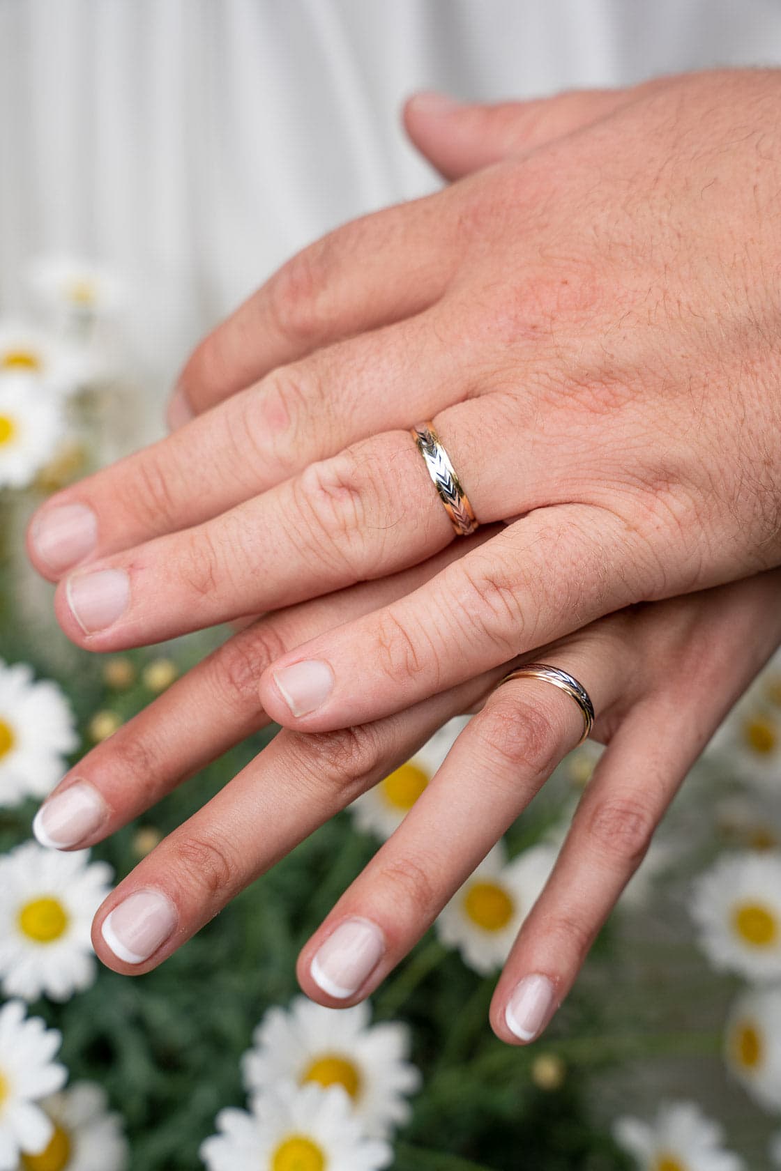 Mains des mariés montrant leurs alliances entourées de fleurs blanches
