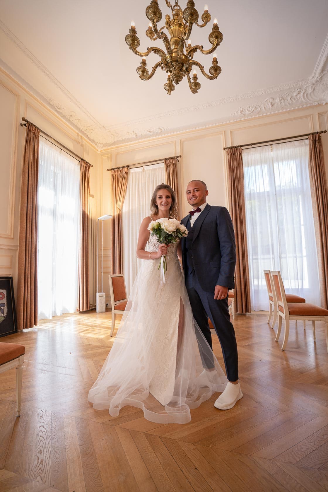 Portrait des mariés dans une élégante salle de mairie avec un lustre en arrière-plan