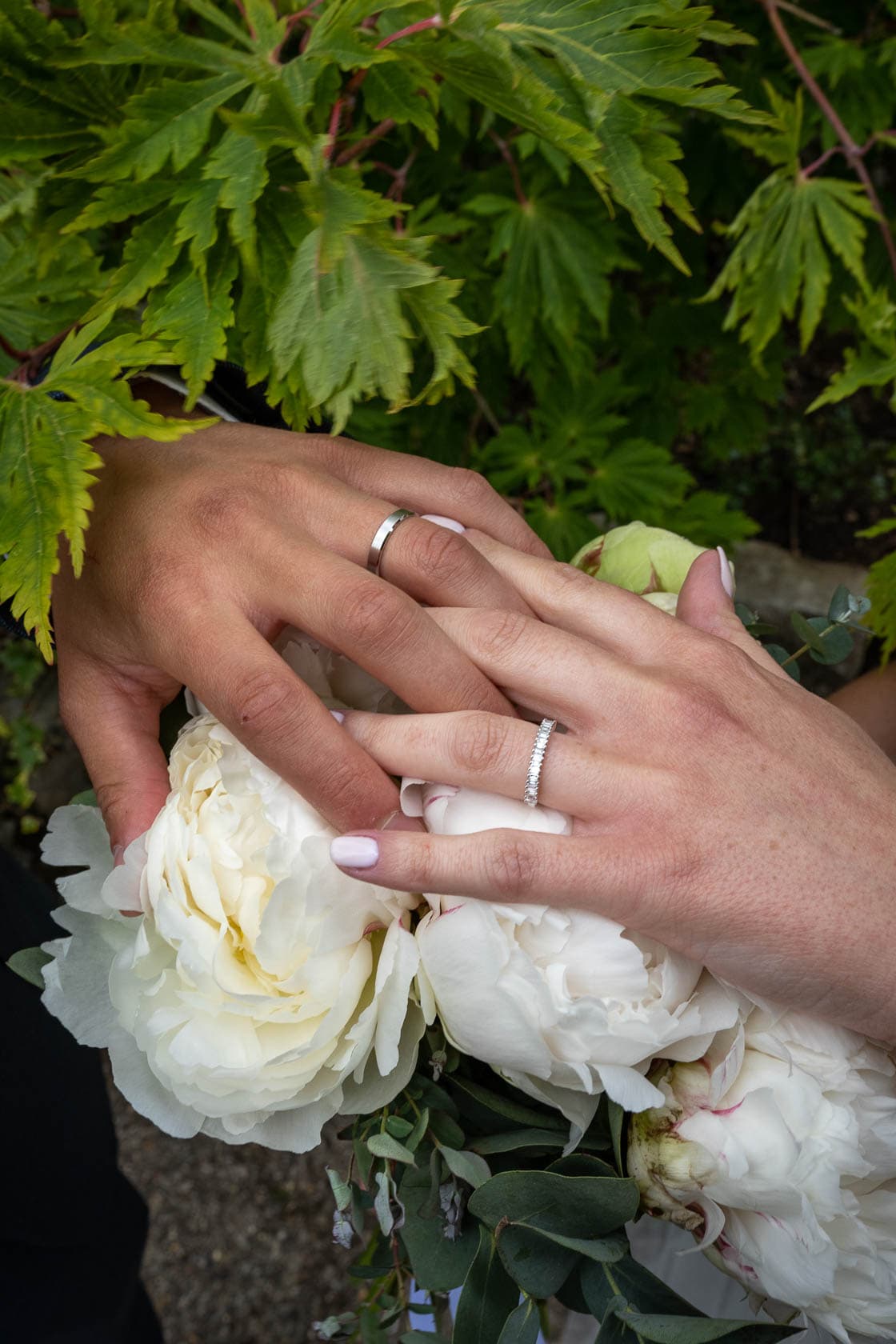 Mains des mariés avec leurs alliances et un bouquet de fleurs blanches