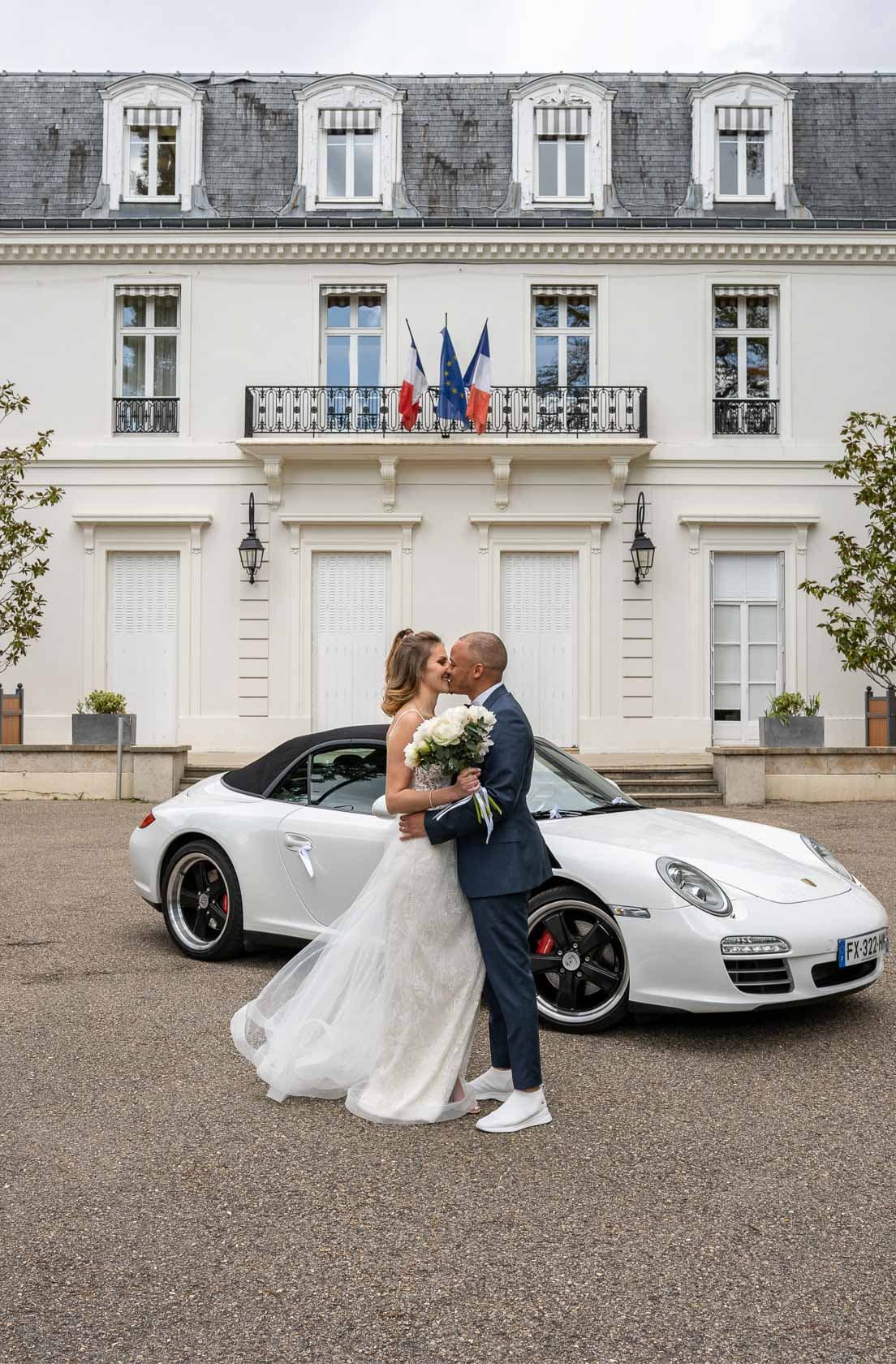 Les mariés posant devant une voiture décapotable blanche devant la mairie de Garches