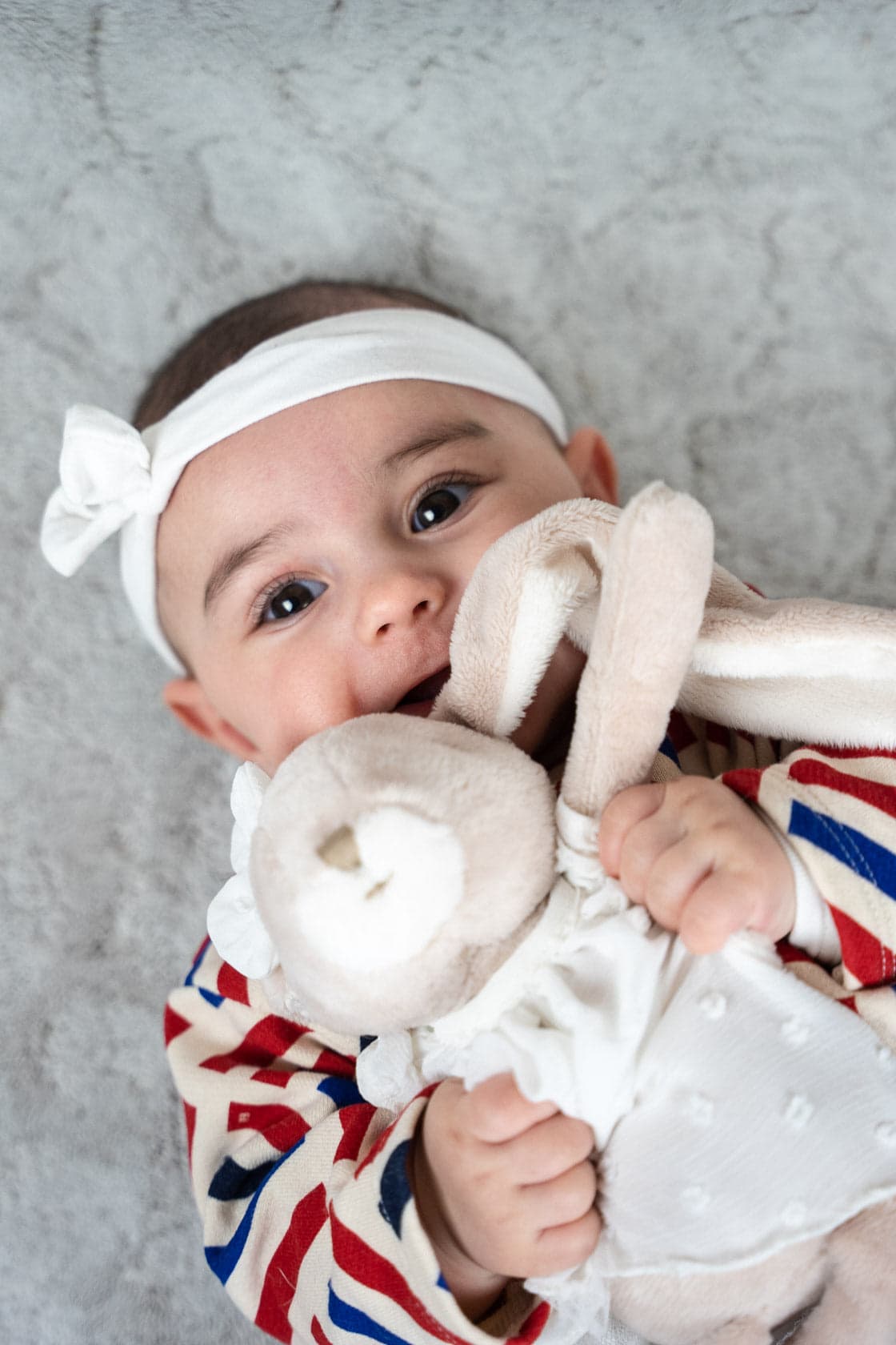 Portrait en gros plan d'un bébé avec un bandeau blanc, mordillant un doudou lapin beige
