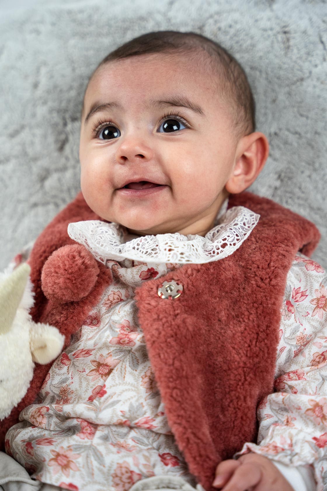 Portrait en gros plan d'un bébé souriant, portant un col en dentelle et un gilet en fausse fourrure bordeaux