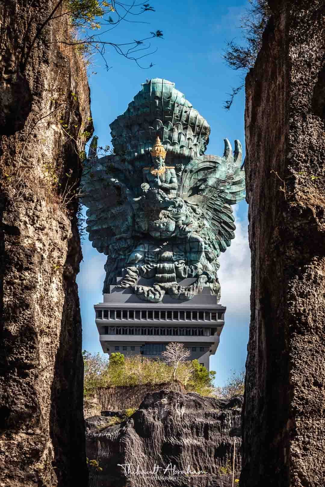 La statue Garuda Wisnu se dresse au loin, cadrée entre deux rochers symétriques, à Bali