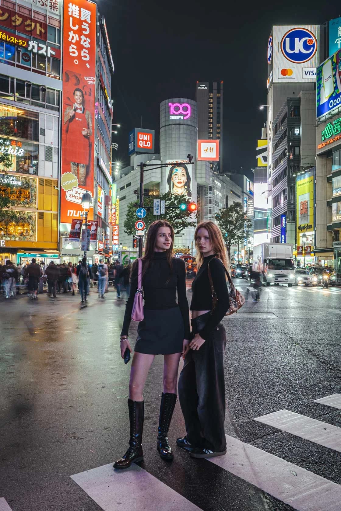 Two friends in boots and wide-legged trousers, standing on the Shibuya pedestrian crossing