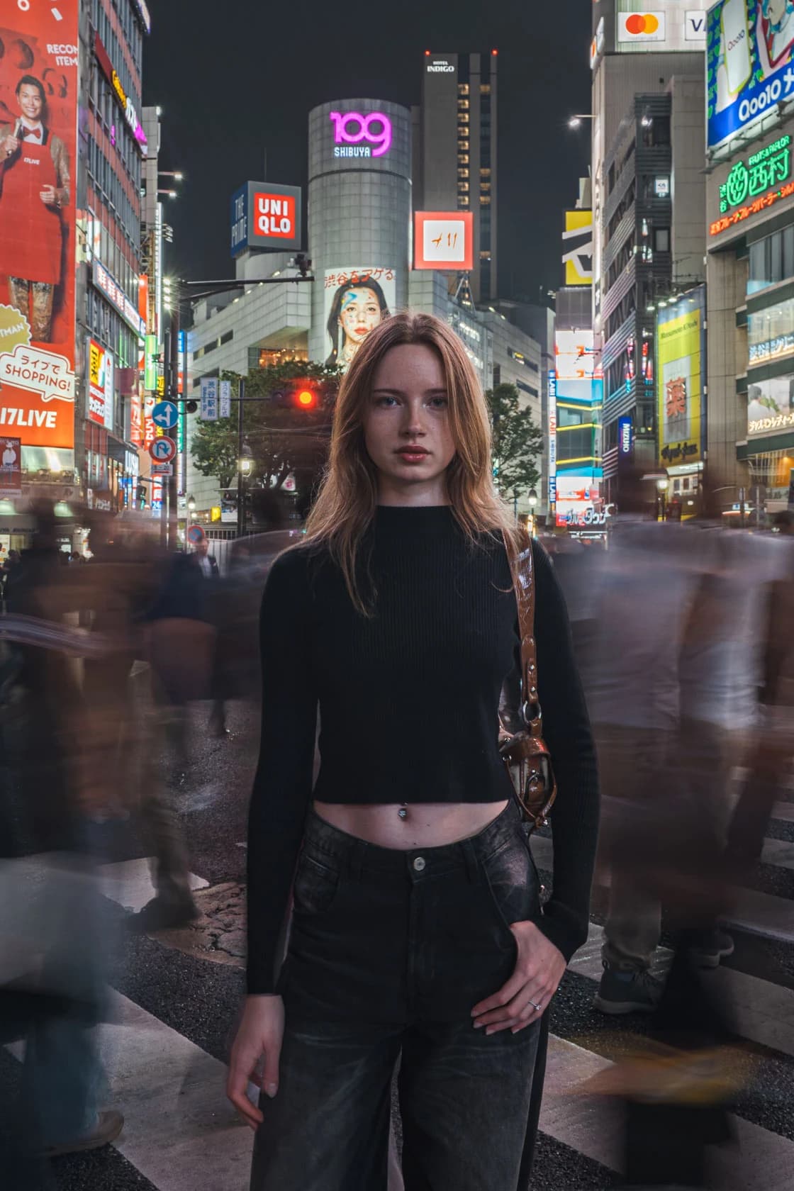 Mannequin en pull noir, sac bandoulière en cuir, portrait à mi-corps devant les enseignes de Shibuya