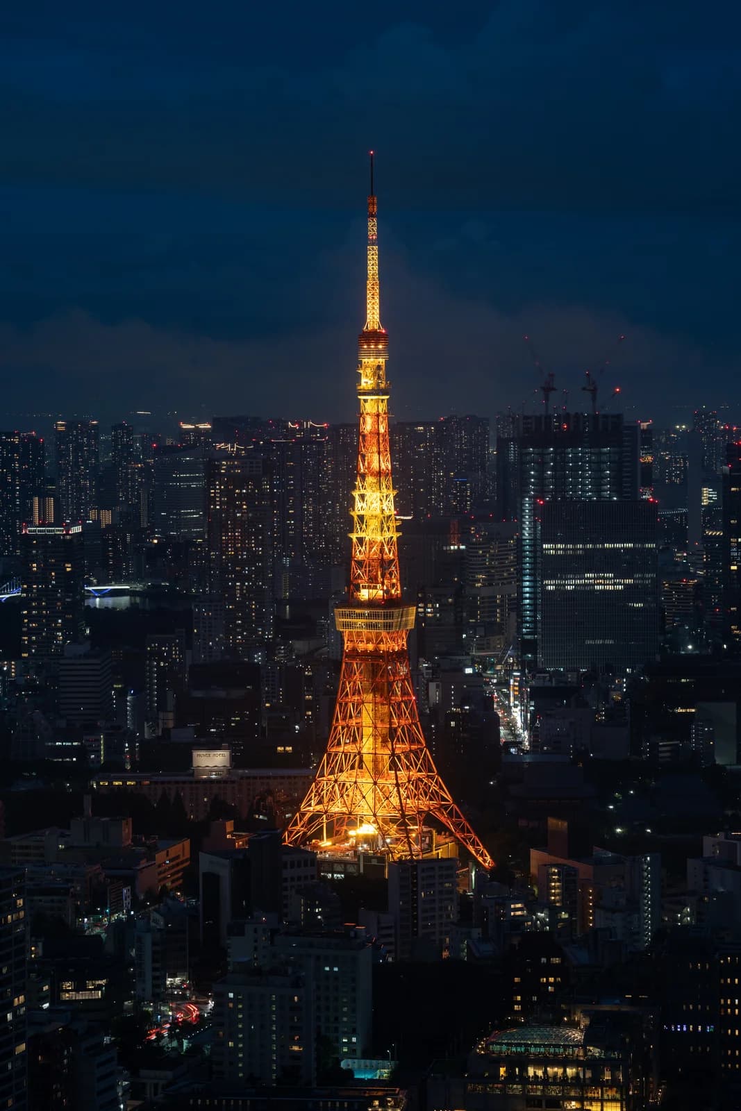 Tour de Tokyo illuminée en orange de nuit, dominant le skyline de la ville avec ses gratte-ciel éclairés