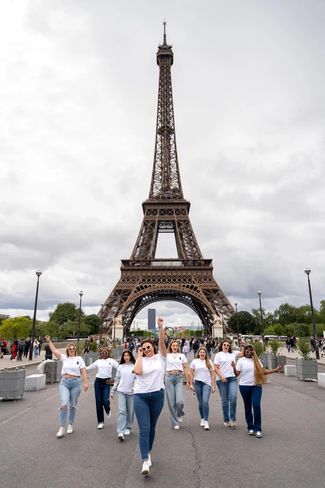 Group of friends walking towards the camera, one hand raised in a victory sign, Eiffel Tower in the background