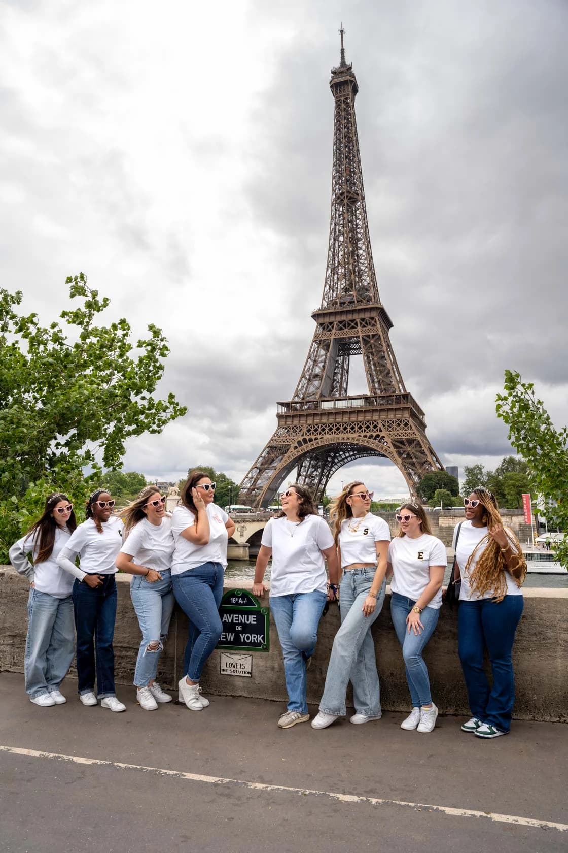 A group of friends leaning on the parapet of the Pont d'Iéna, laughing together, with the Eiffel Tower in the background.