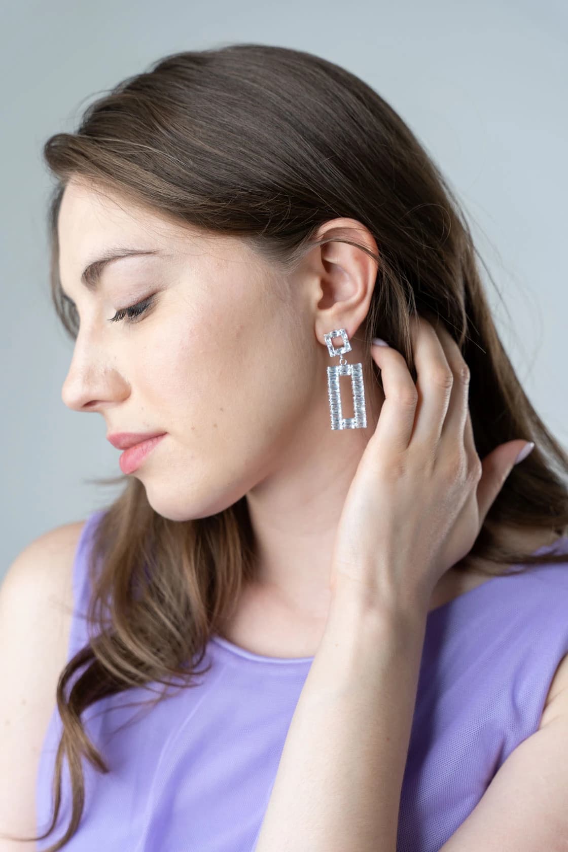 Femme brune de profil, boucles d'oreilles argentées géométriques, main dans les cheveux