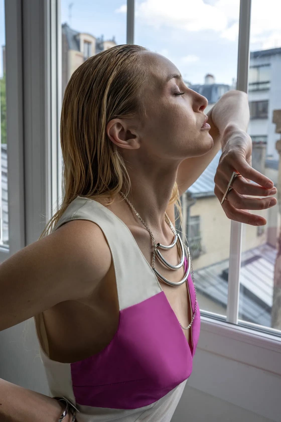 Mannequin en bijoux argentés superposés, devant une fenêtre parisienne