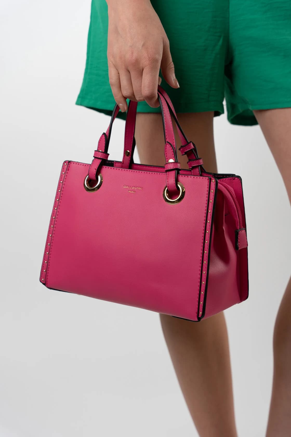 Sac cabas rigide rose fuchsia à clous dorés, tenu à la main
