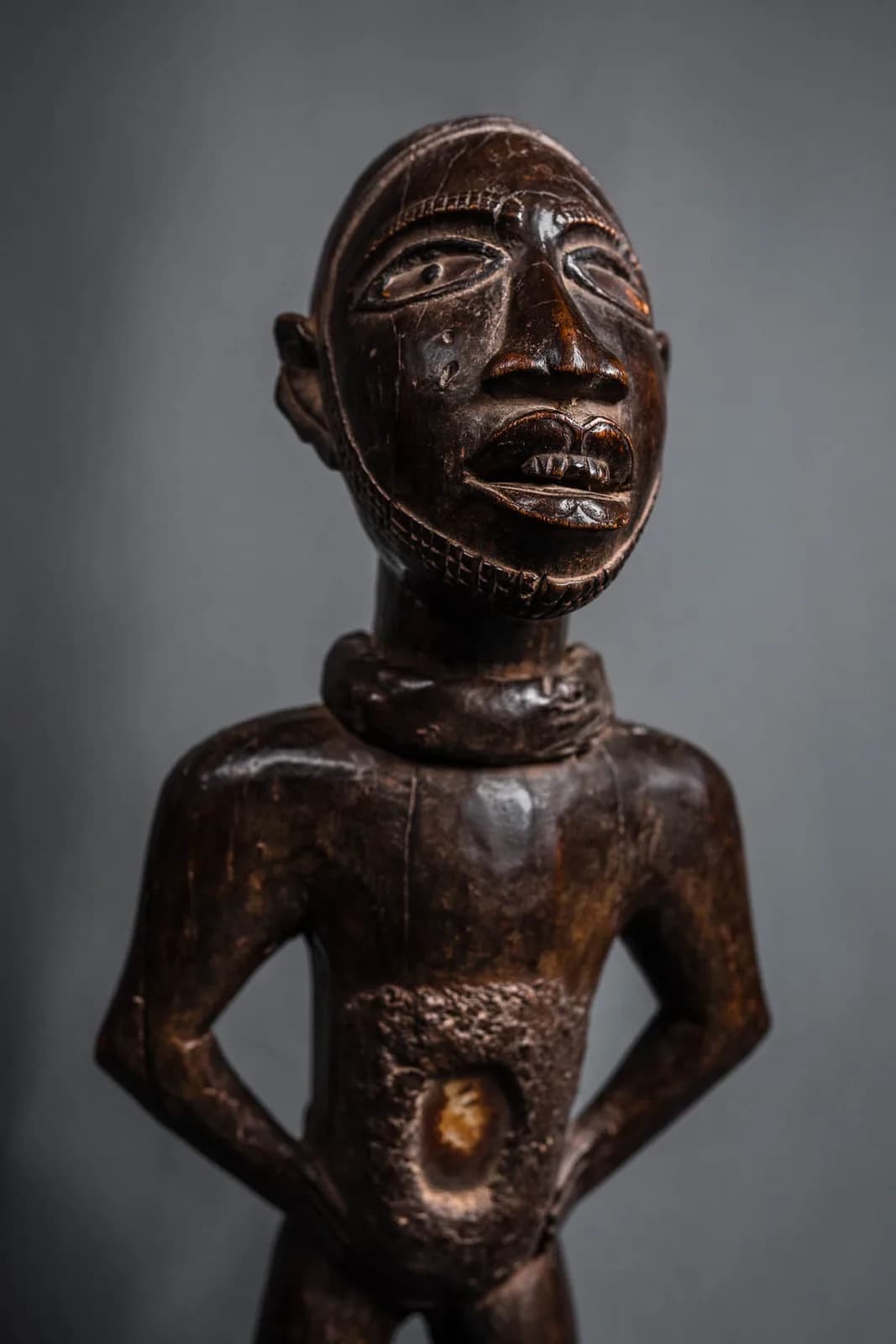 Statuette africaine en bois sculpté représentant un buste d'homme, scarifications au visage, fond gris studio