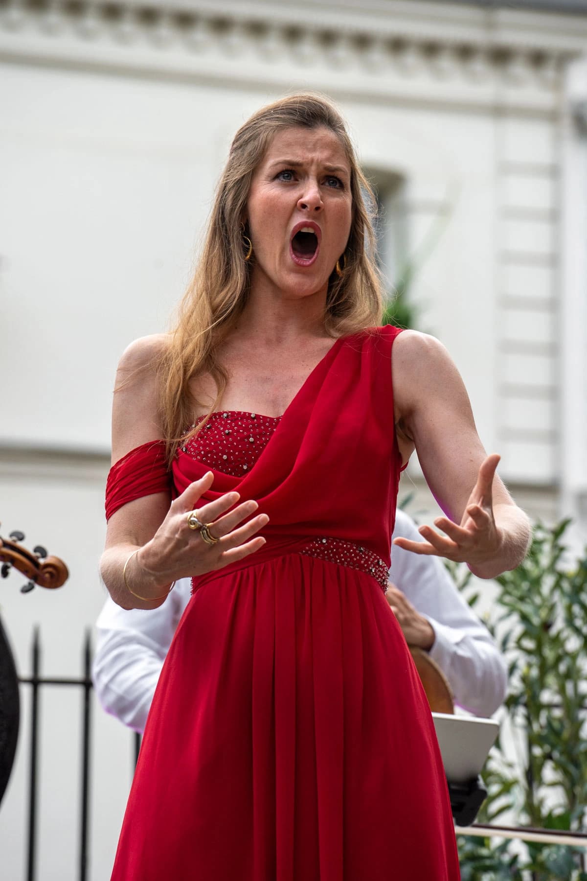 Chanteuse soprano en robe rouge, bras ouverts, en pleine intensité vocale, Arènes musicales de Montmartre