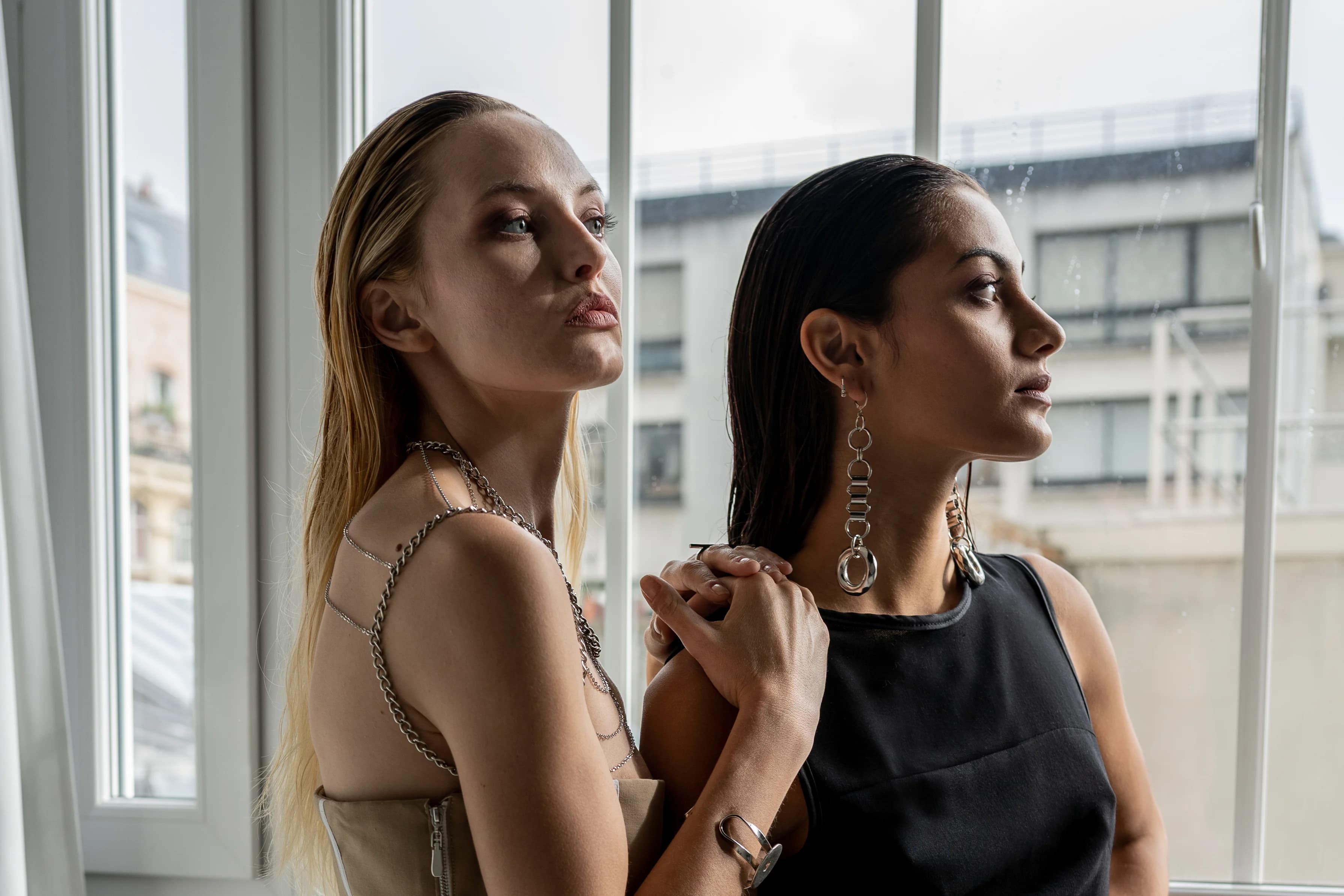 Duo de mannequins de profil, bijoux argentés, devant une fenêtre parisienne